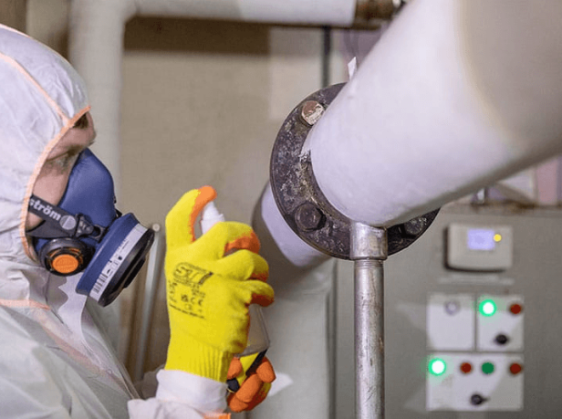 Licensed operative in full PPE inspecting and treating asbestos pipe lagging on a heating system in a Surrey commercial property
